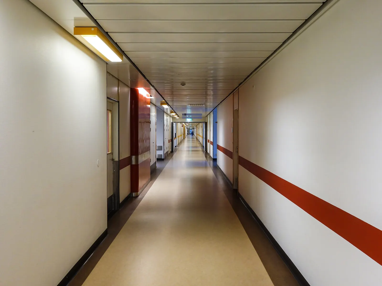 A long, empty hospital corridor with closed doors and a red stripe along the wall